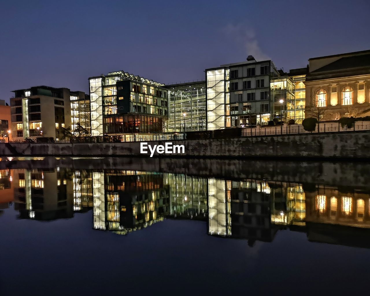 Reflection of illuminated buildings in river against sky at night