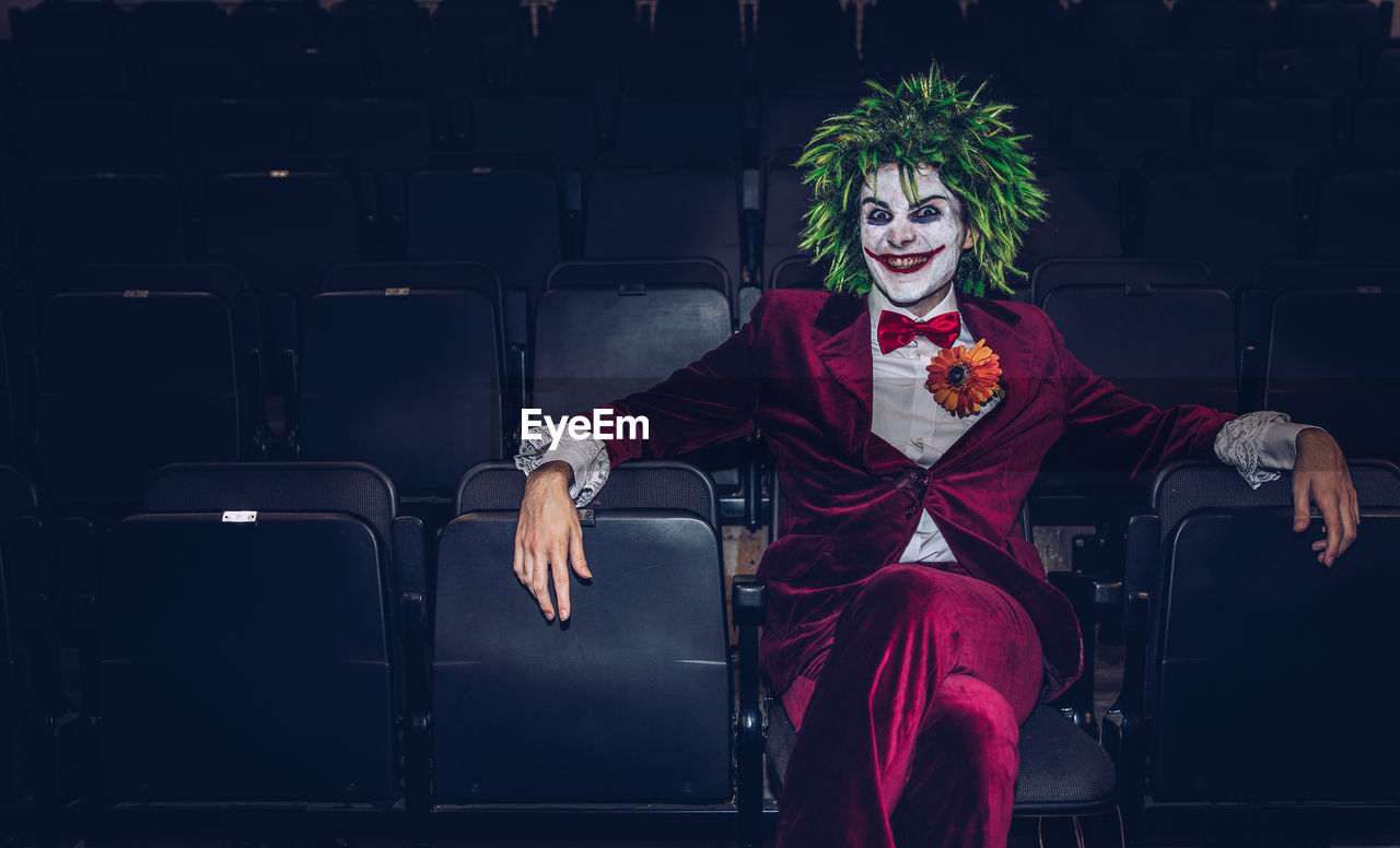 Portrait of man wearing clown costume sitting on chair