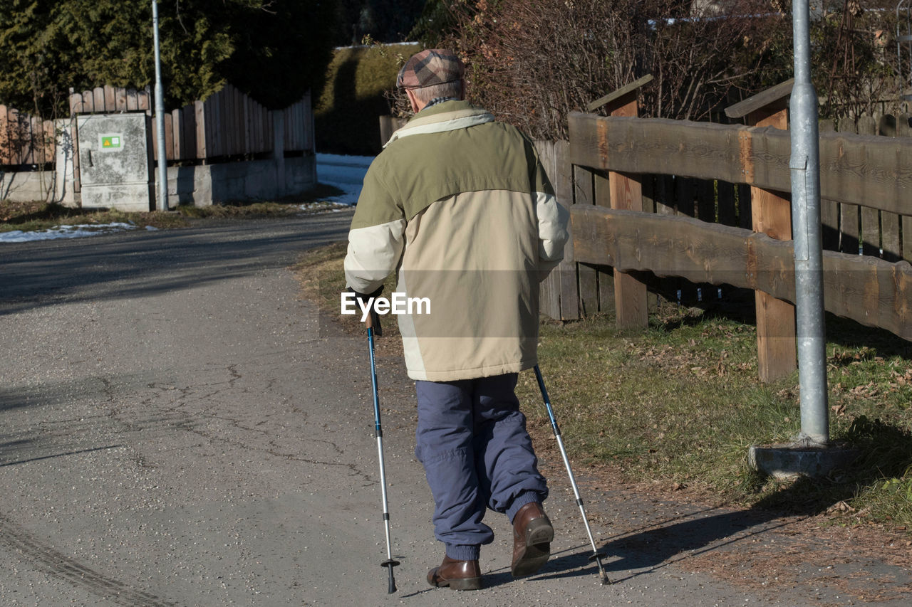 REAR VIEW OF MAN WALKING ON FOOTPATH BY CITY