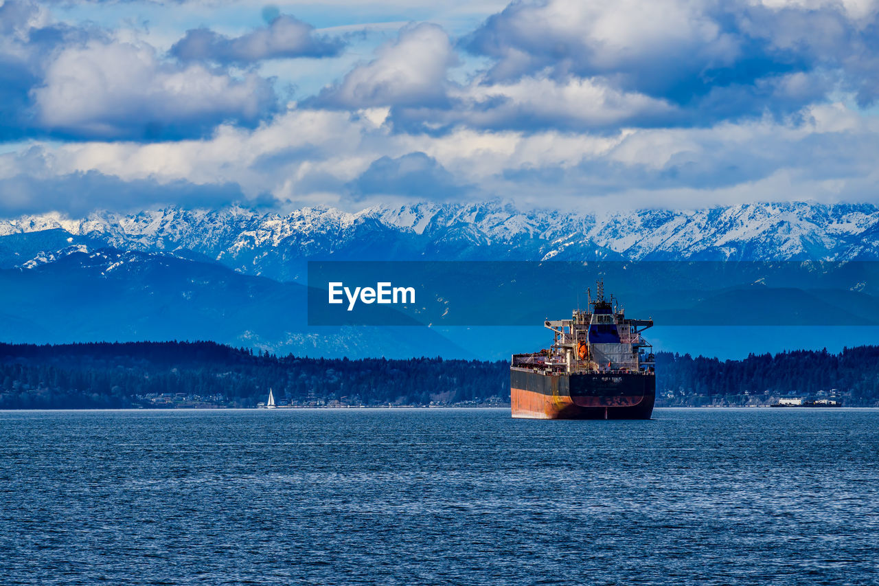 A tanker ship in elliott bay with the olympic mountain range in the distance.