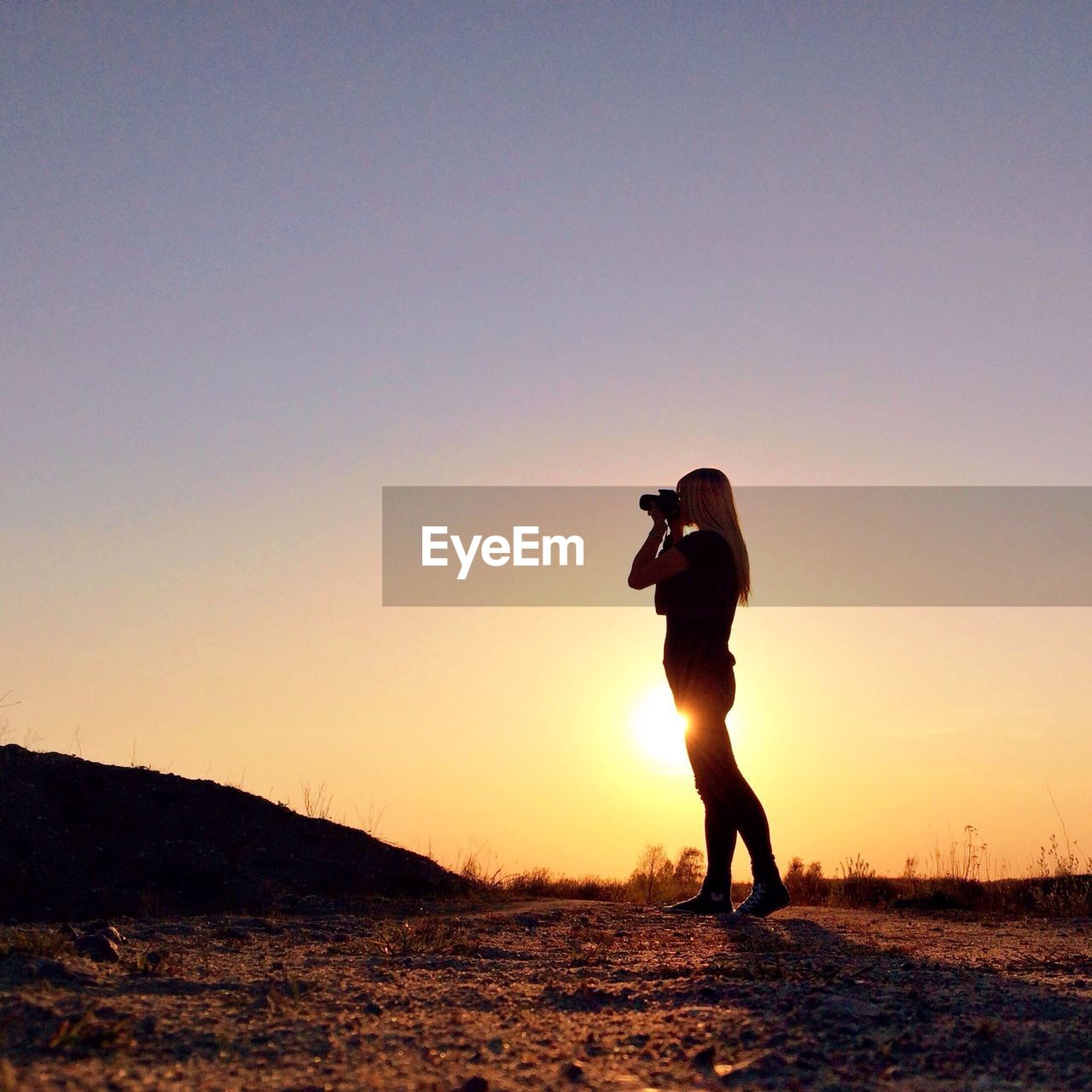 Silhouette woman photographing landscape at sunset