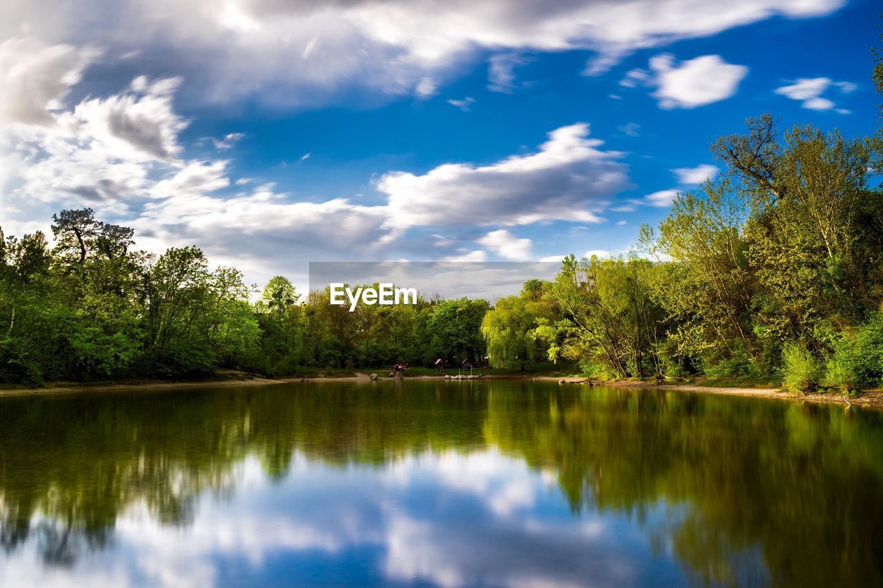 Idyllic shot of green trees reflection in lake against sky