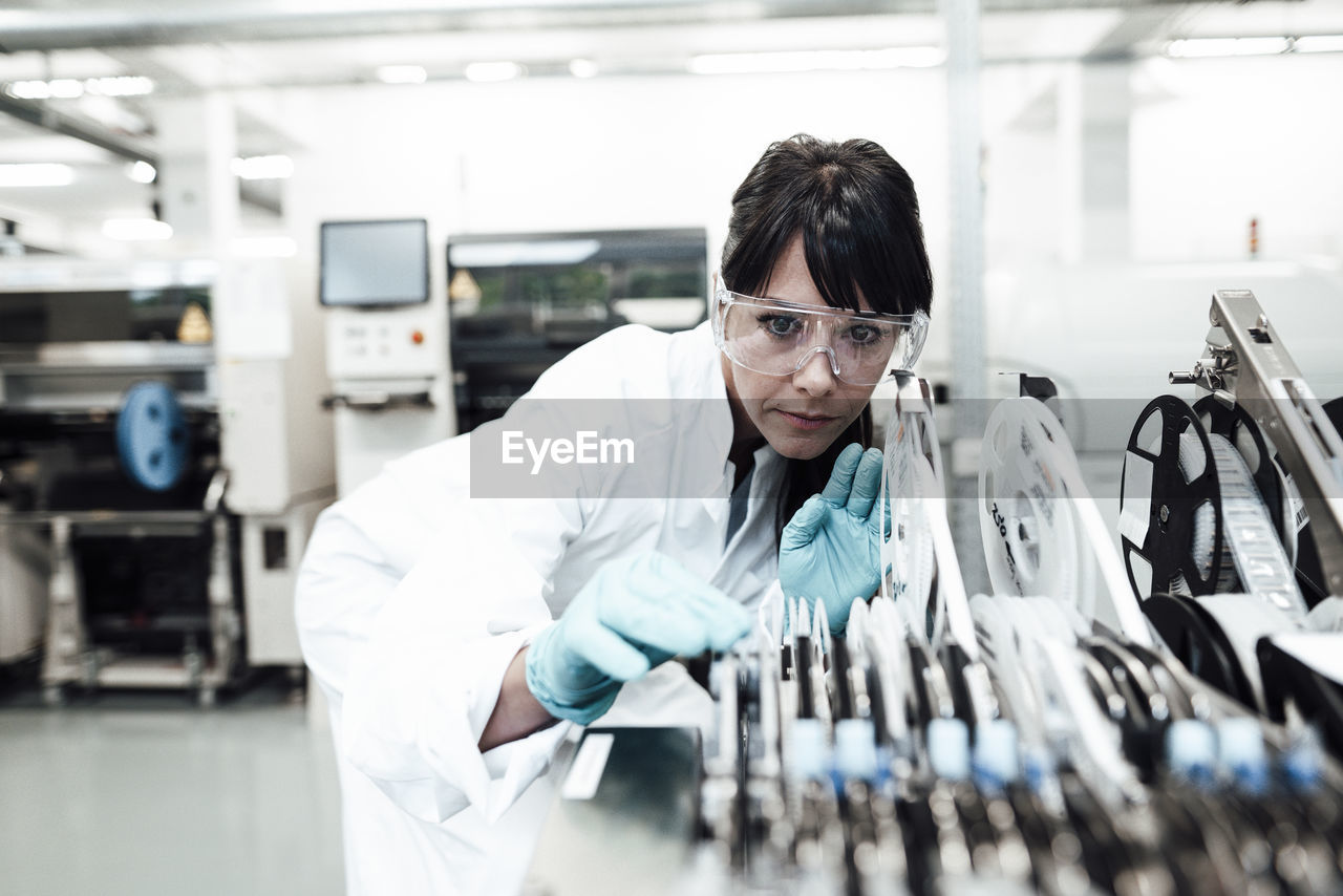 Mature female technician examining machinery in bright industry