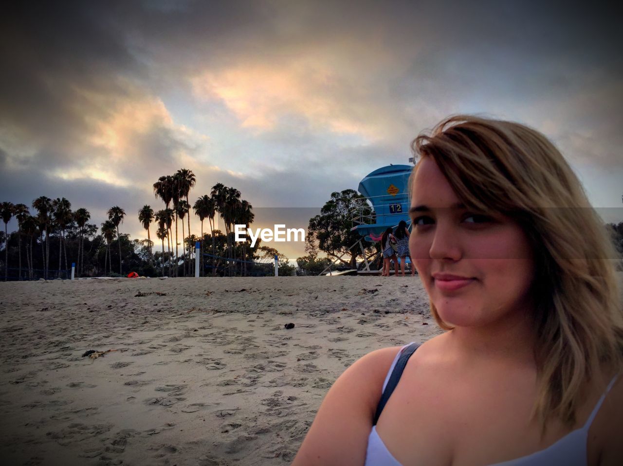 Close-up portrait of woman standing at beach against cloudy sky