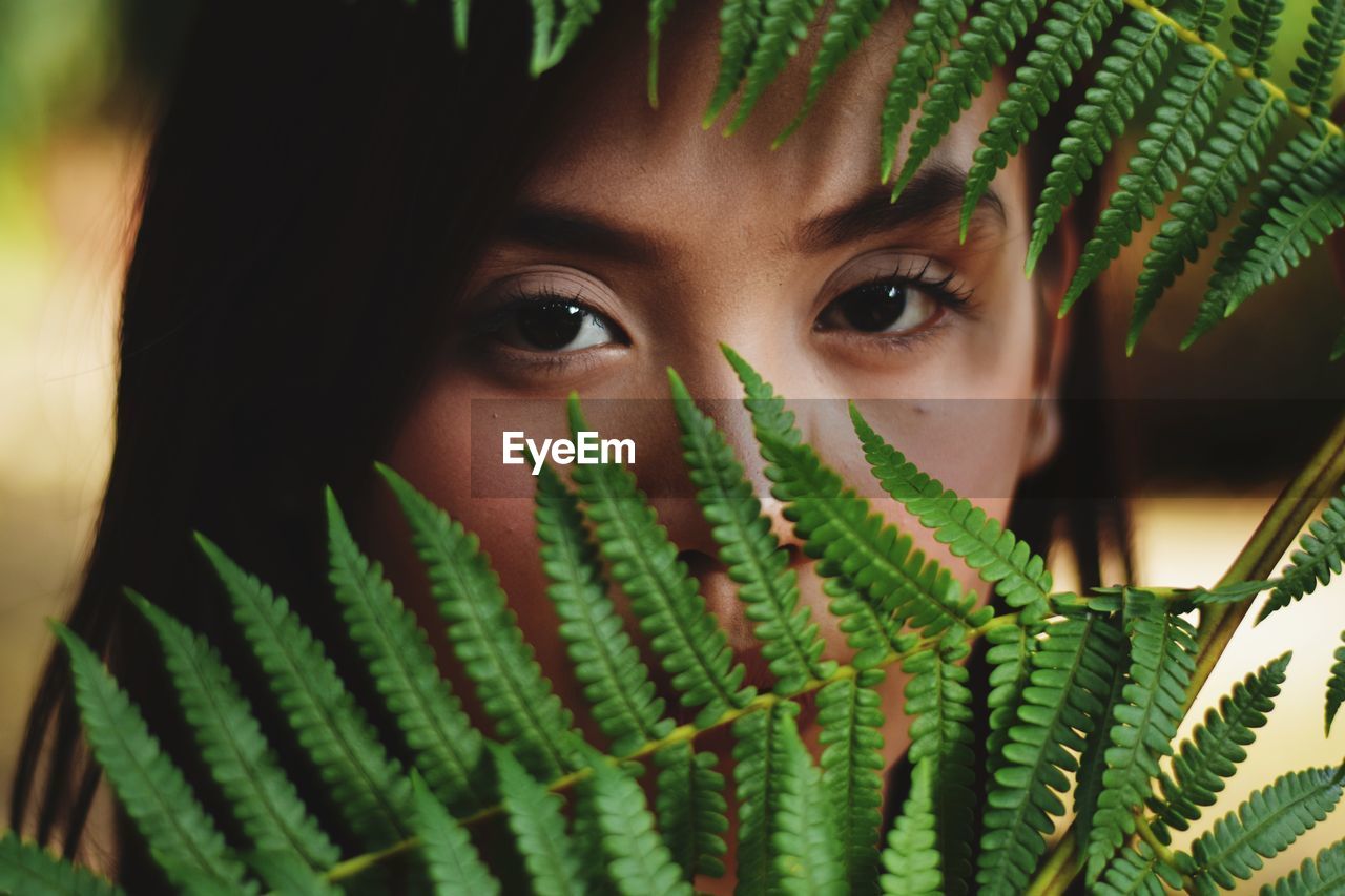 Close-up portrait of young woman looking through plants