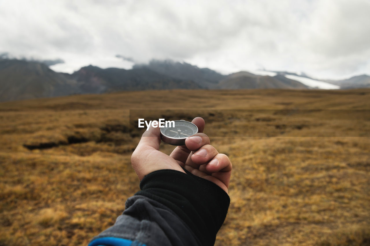 A man's hand of a traveler holds a magnetic compass against the background of a mountain landscape 
