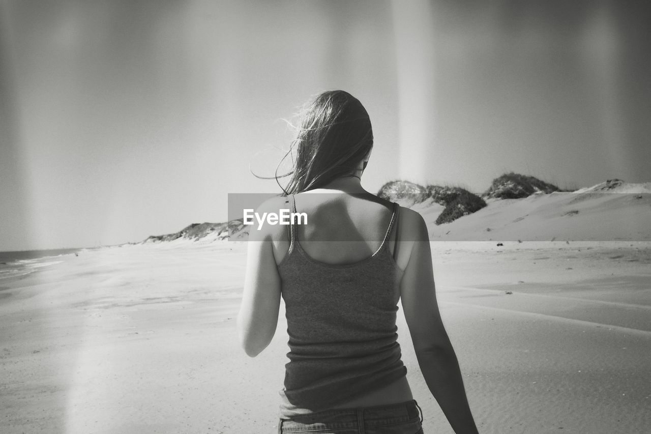 REAR VIEW OF WOMAN STANDING AT BEACH