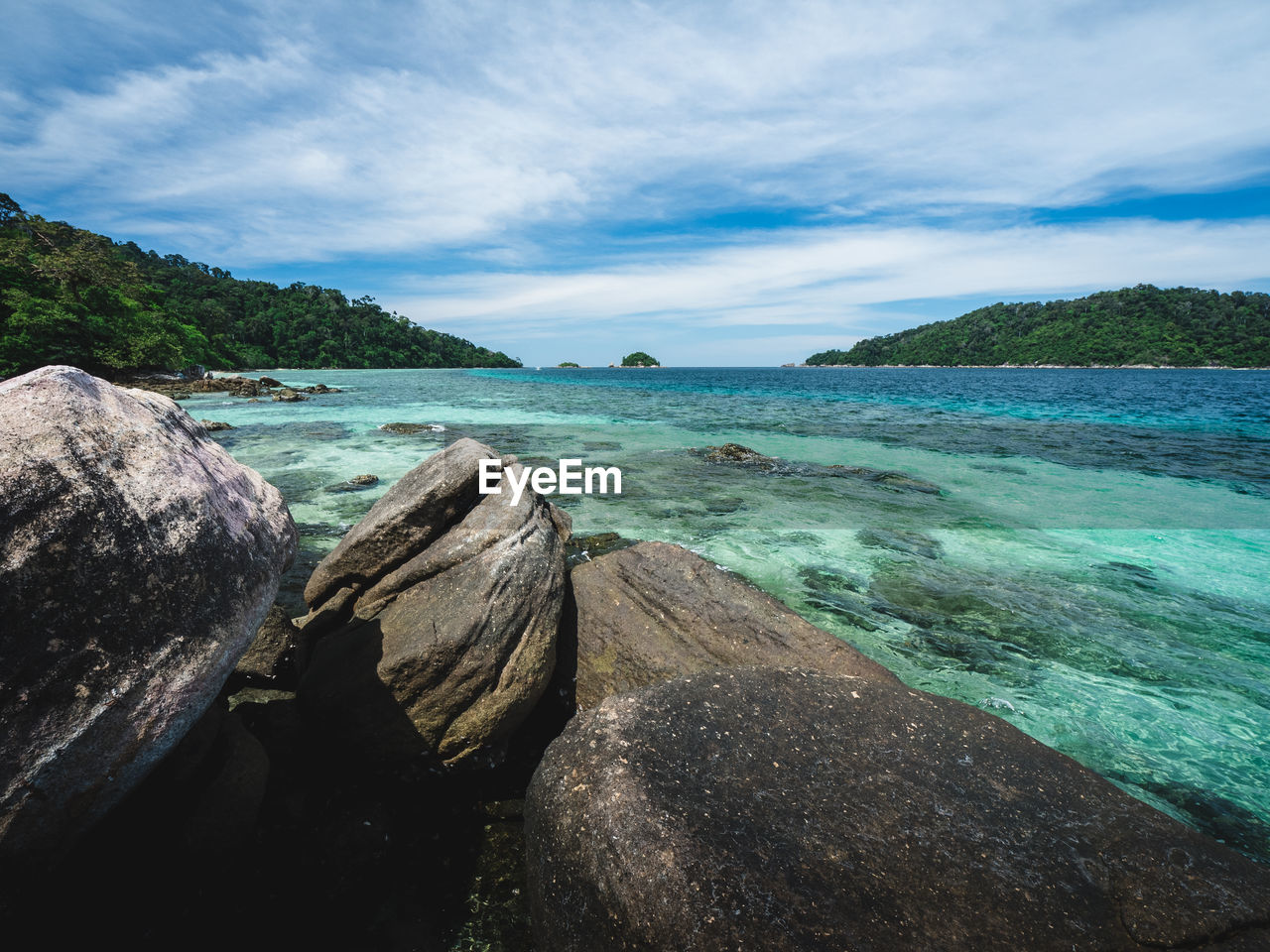 Scenic view of clear turquoise sea and rocky beach against blue sky near koh lipe island, thailand.
