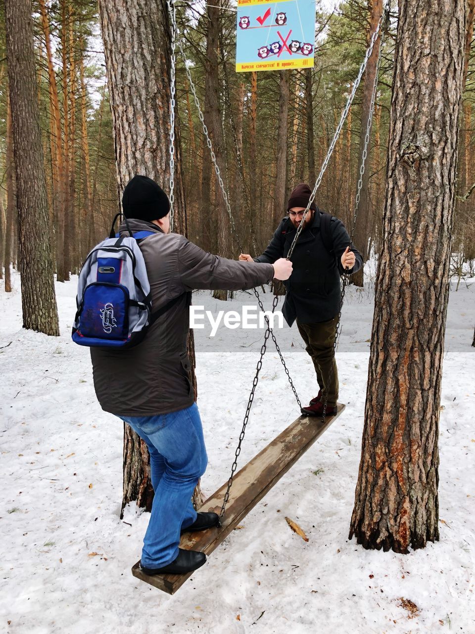 REAR VIEW OF MAN STANDING ON TREE TRUNK