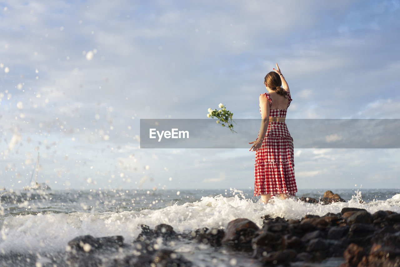 Rear view of woman standing on rock by sea against sky