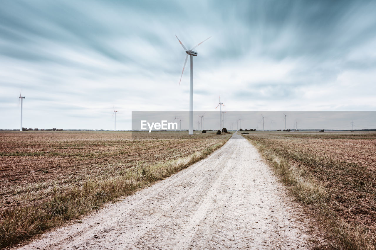 Country road passing through a field with wind turbines