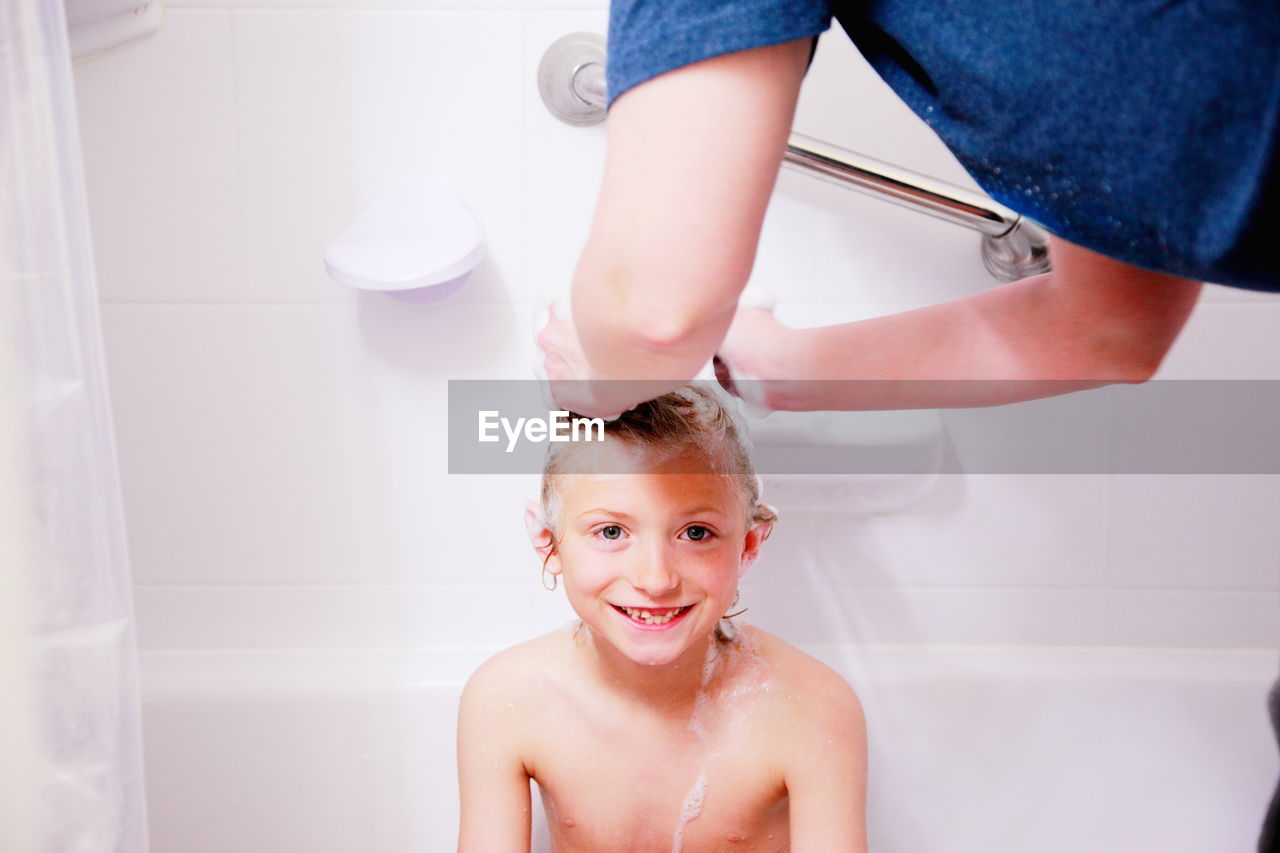 Cropped image of woman bathing son in bathtub