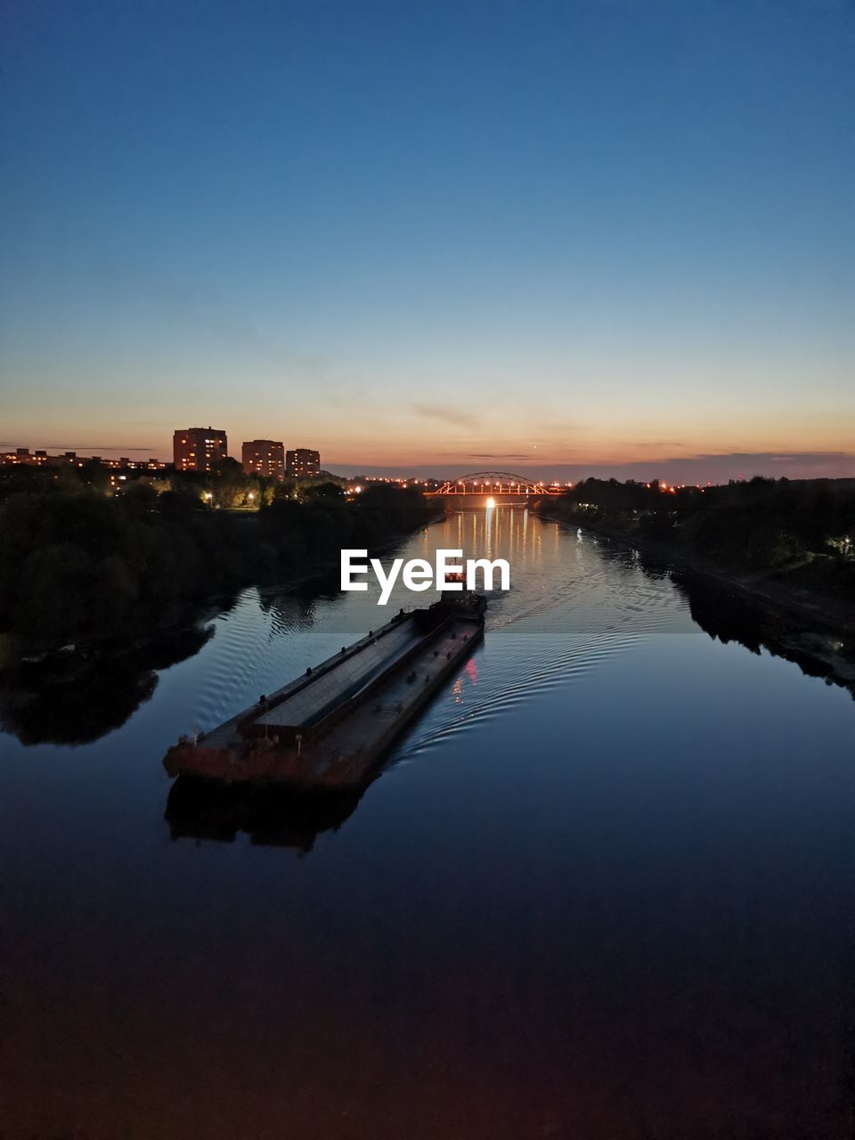 ILLUMINATED BUILDINGS BY LAKE AGAINST SKY AT SUNSET