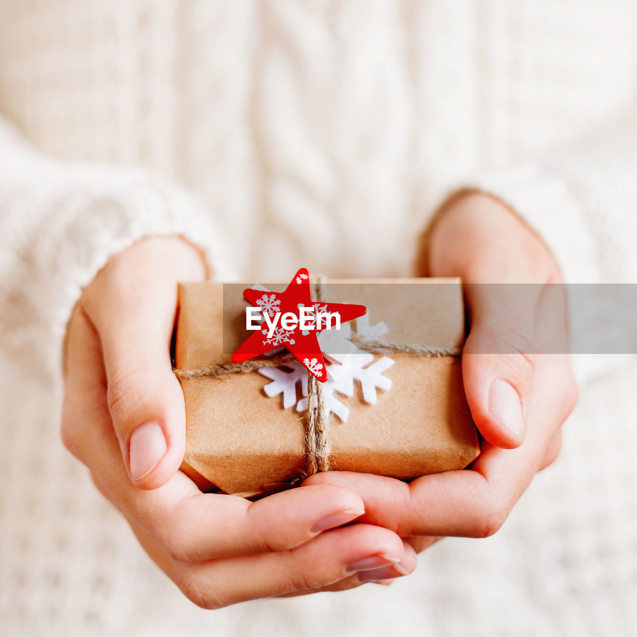 Woman in knitted sweater is holding christmas present with felt snowflake and red star.