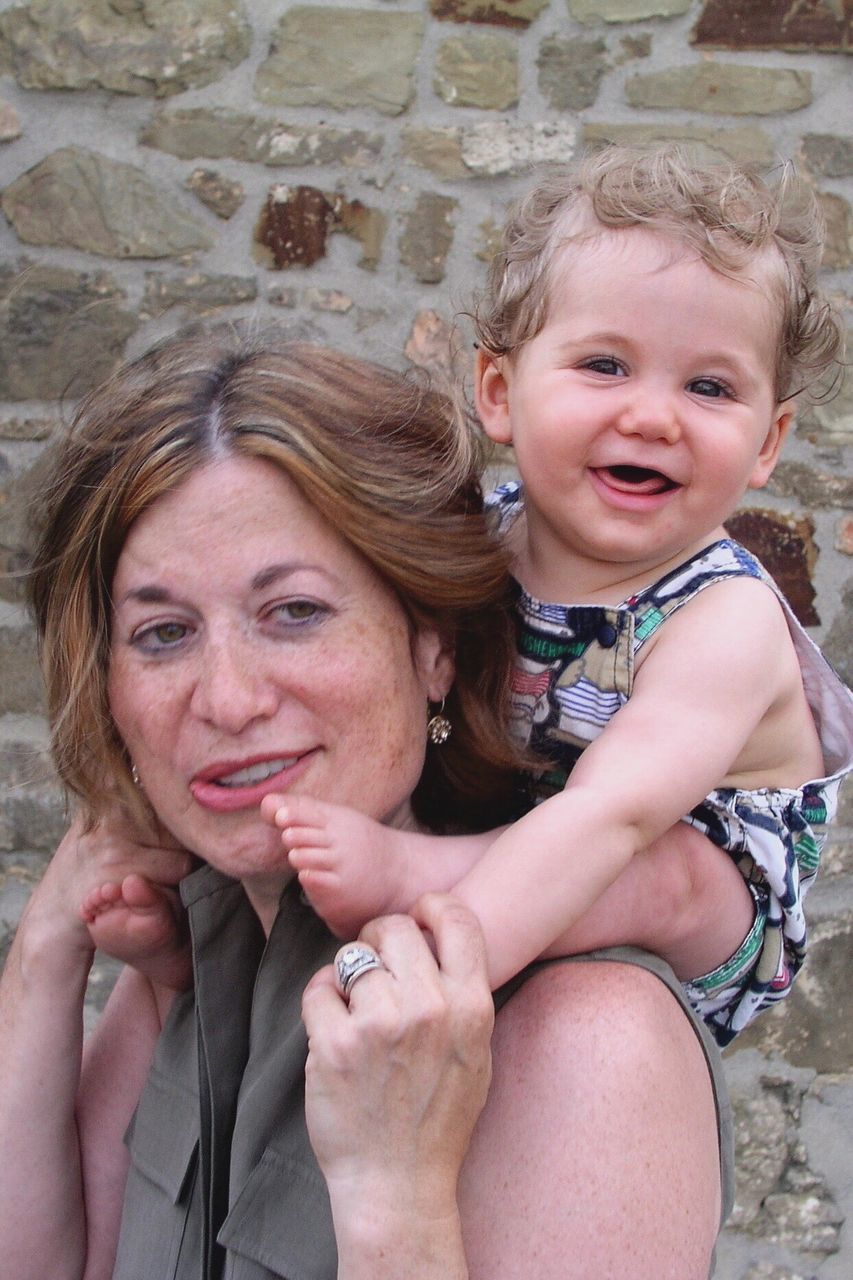 Mother carrying baby boy on shoulder against stone wall