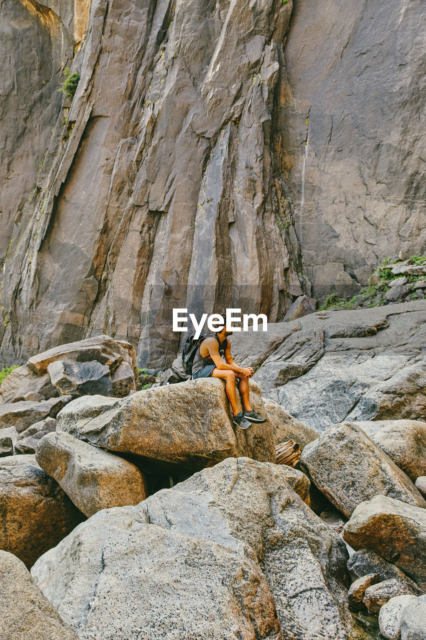 Young man resting on boulder, observing yosemite falls.