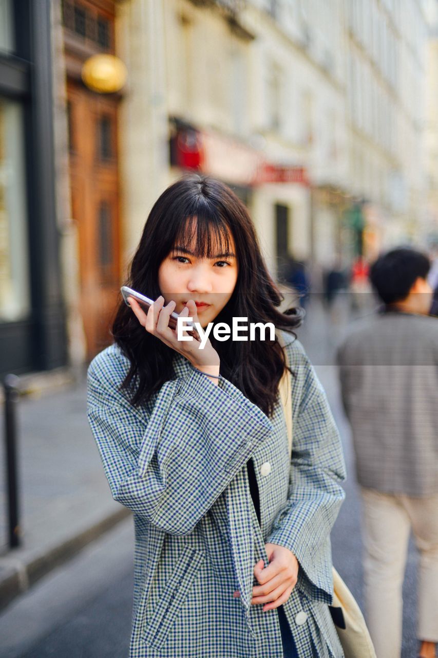 Portrait of young woman holding mobile phone while standing outdoors