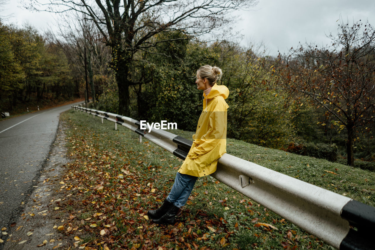 A serene middle-aged woman in a yellow raincoat walks in rainy weather in the countryside.