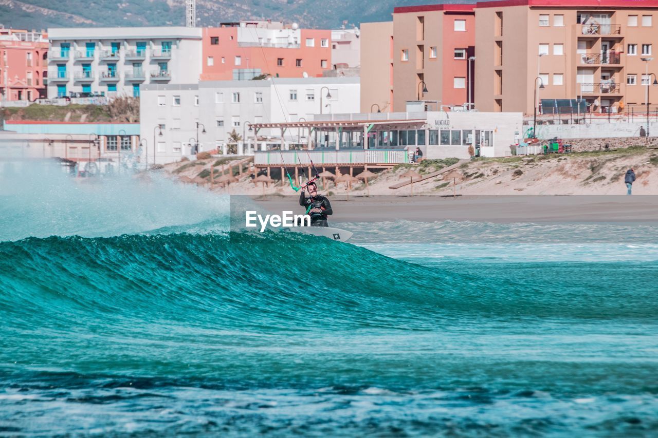 Man kitesurfing in sea against buildings in city