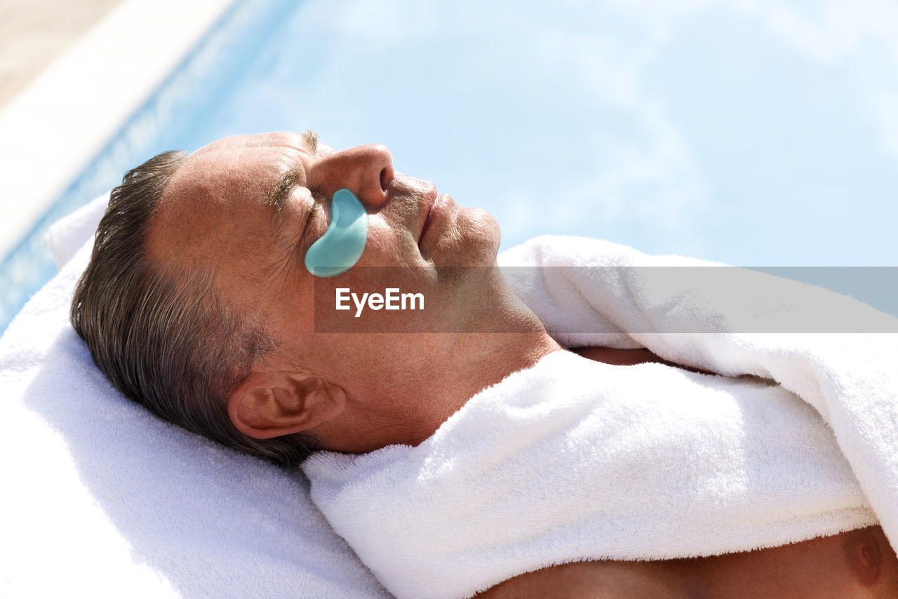 Mature man with collagen patch below eye at pool spa