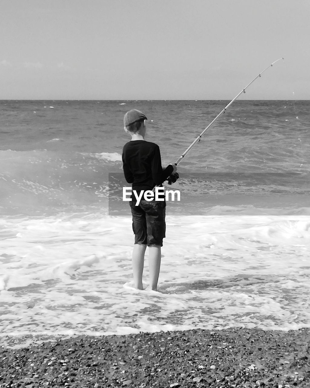 Rear view of boy standing fishing on the beach