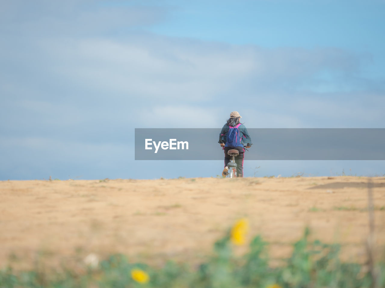 Rear view of woman cycling bicycle on field against sky