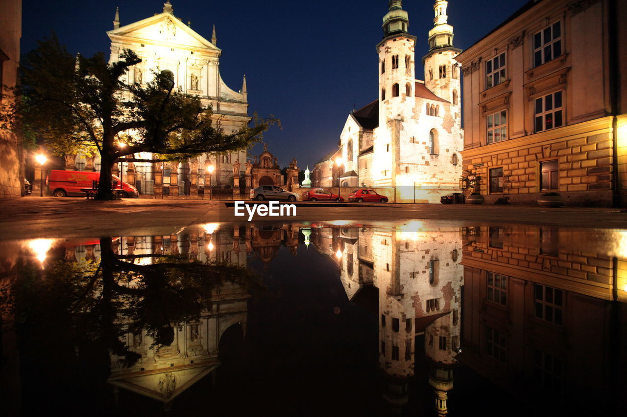 Reflection of illuminated wawel cathedral on puddle at dusk