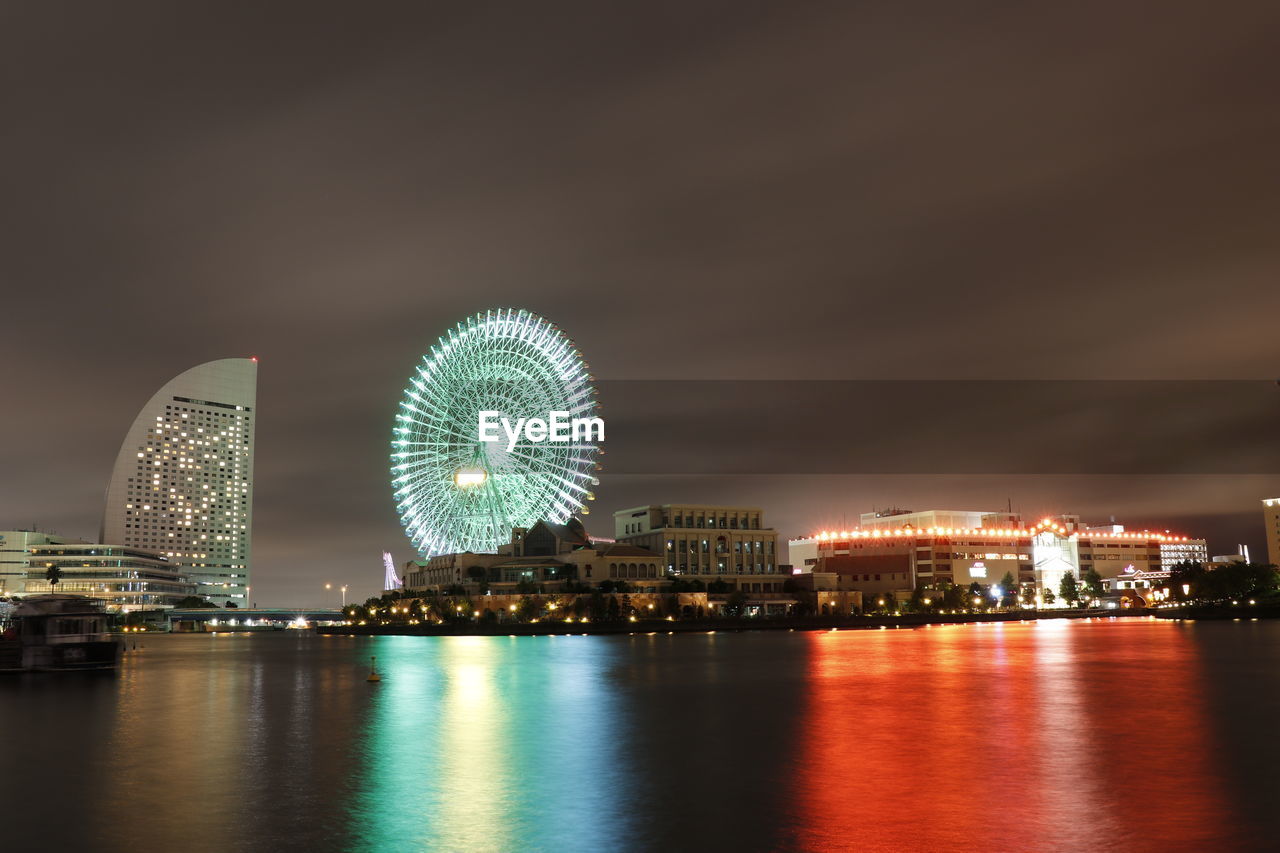 ILLUMINATED FERRIS WHEEL BY RIVER AGAINST SKY