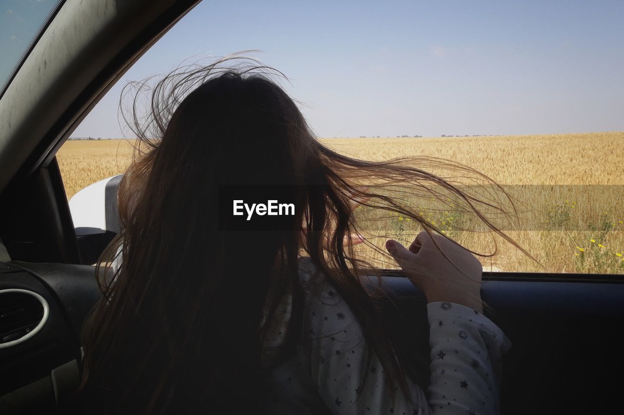 Rear view of girl looking at landscape through car window