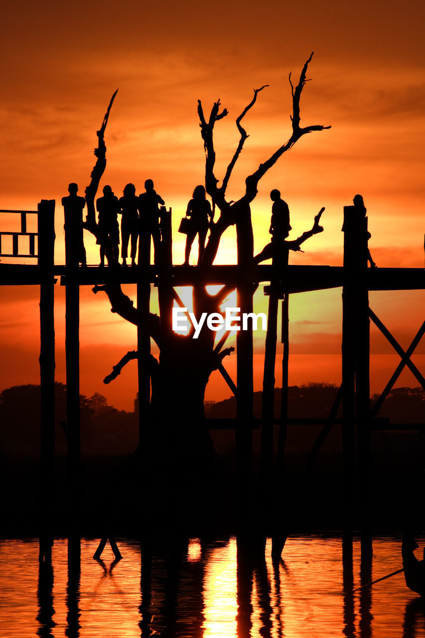 Silhouette people on footbridge against sky during sunset