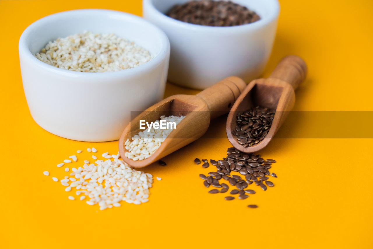 Wooden spoons with sesame and flax seeds lies in a white mortar on a yellow background. healthy eat