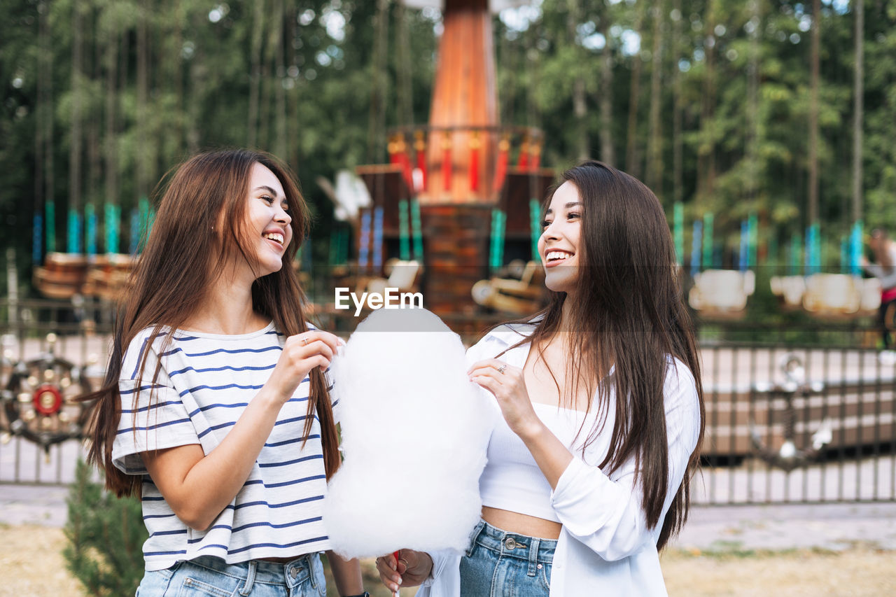 Young women with long hair friends with cotton candy in their hands having fun at amusement park