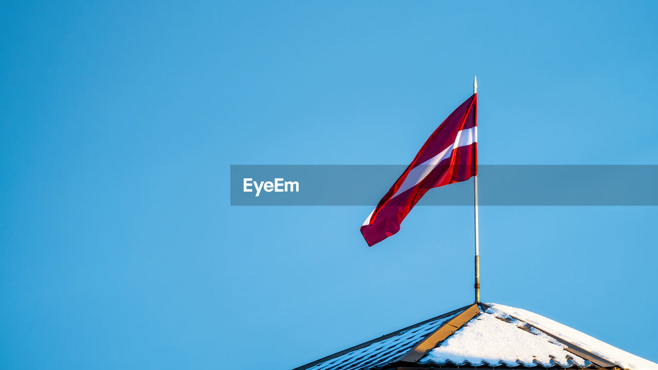 Latvian flag on the flagpole fluttering in the wind against blue clear sky background, copy space