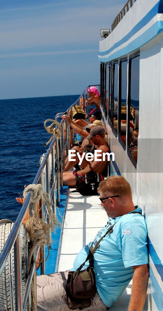 PEOPLE STANDING ON BOAT SAILING IN SEA