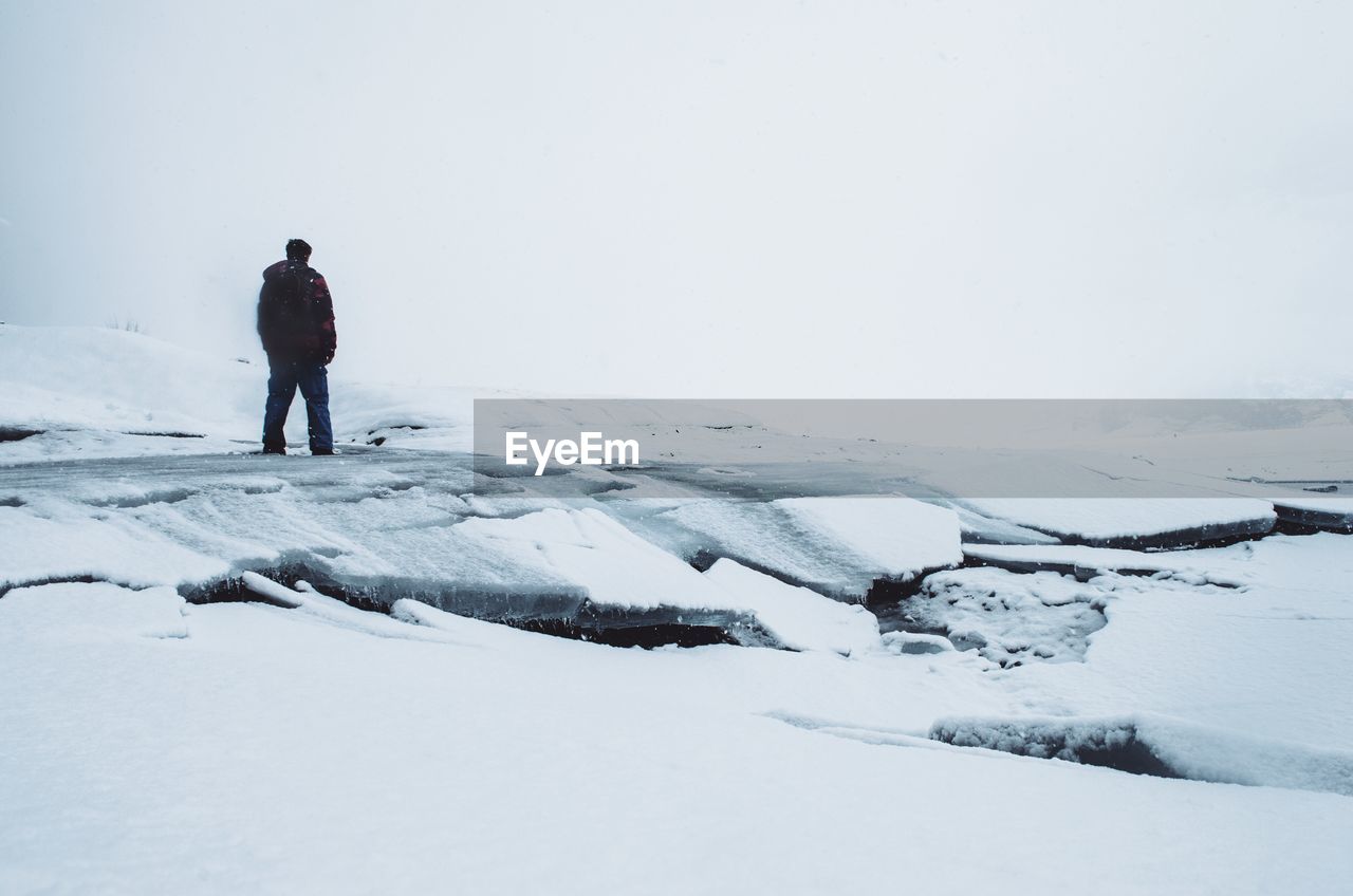 Full length rear view of man standing on snow covered field