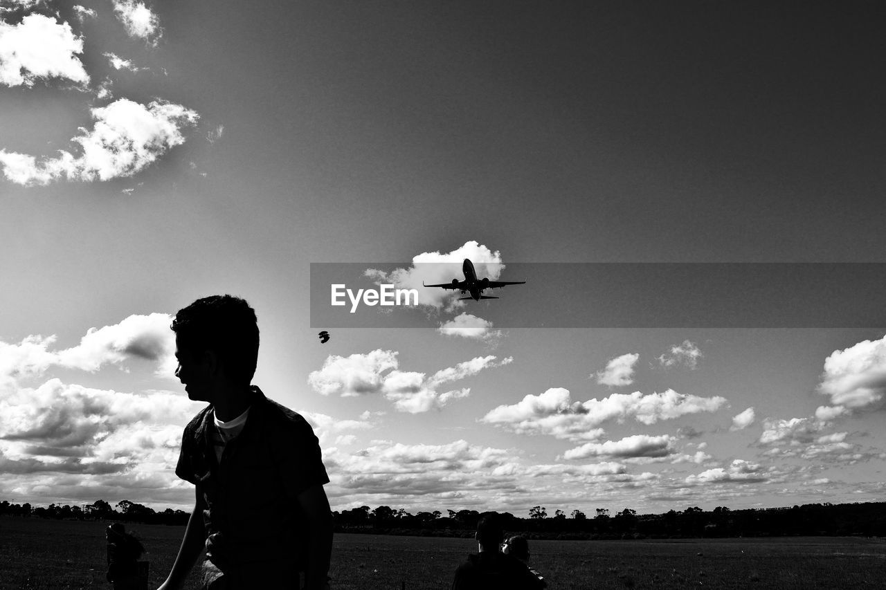 Playful boy on field against airplane flying in sky