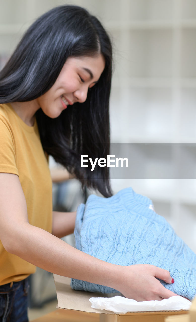 A woman is packing a sweater in a box for shipping.