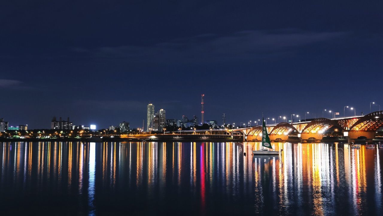 ILLUMINATED CITY BY RIVER AGAINST SKY