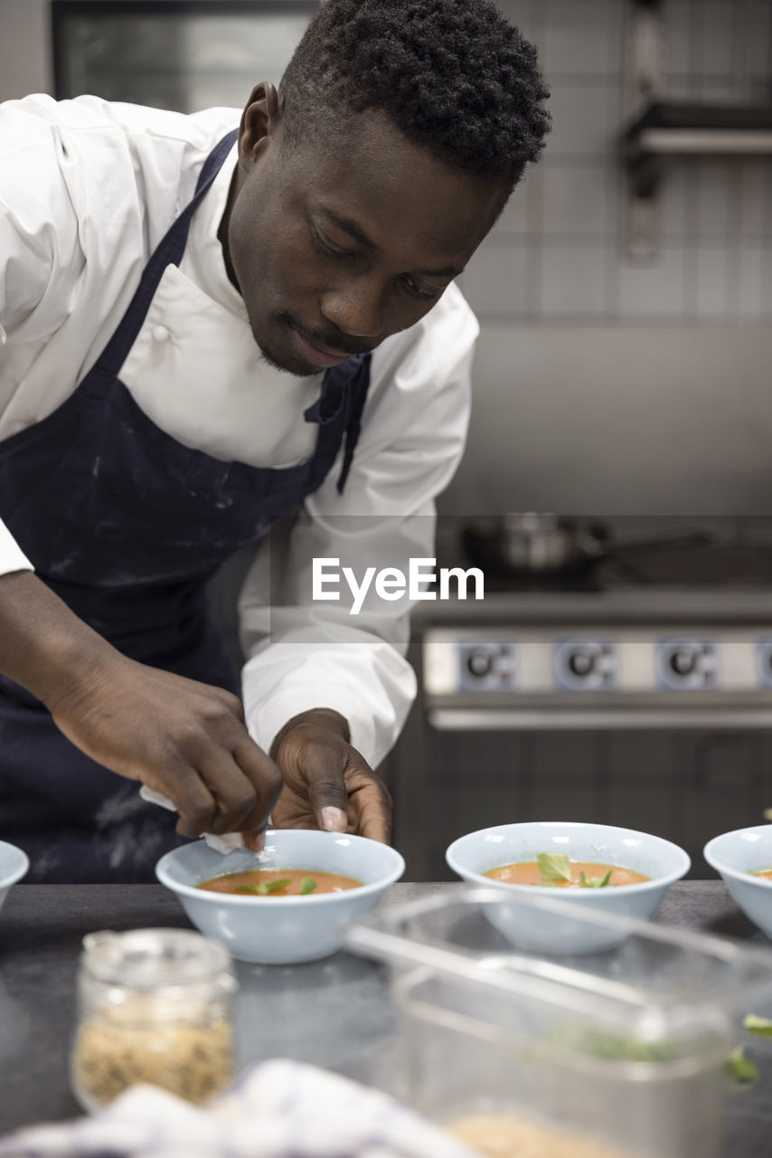 Male chef wiping bowl of soup while working at restaurant