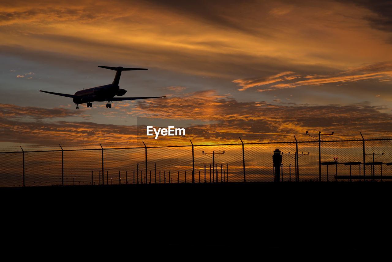 Silhouette airplane flying over runway against sky during sunset