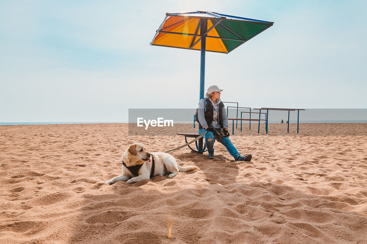 A tourist girl is resting with a dog under a chaise longue on an empty lonely beach