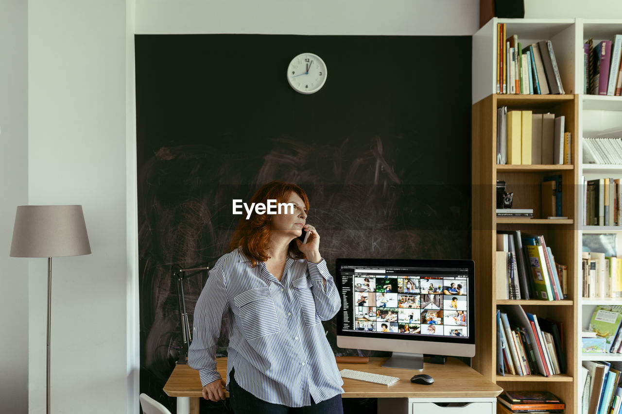 Woman talking on mobile phone while standing by desk at home