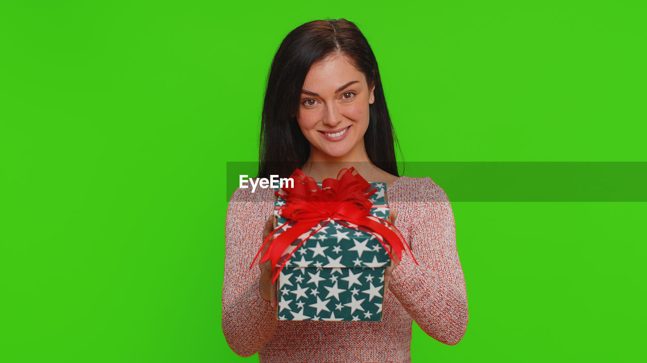 one person, smiling, women, portrait, colored background, adult, happiness, green, studio shot, emotion, looking at camera, indoors, clothing, young adult, green background, waist up, front view, hairstyle, person, cheerful, long hair, standing, female, copy space, brown hair, positive emotion, photo shoot, fashion, teeth, casual clothing, smile, dress, holding, sleeve, lifestyles, human face