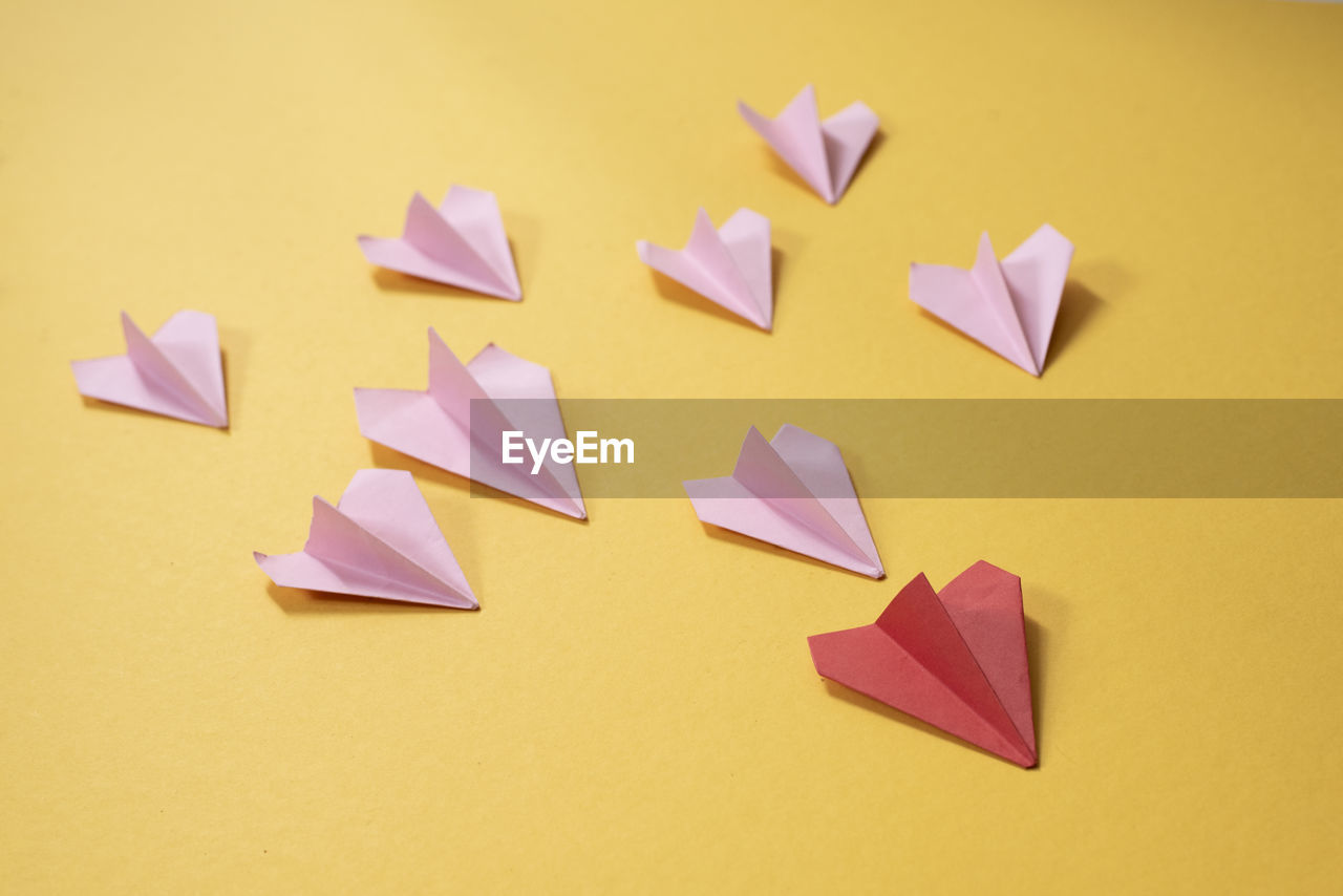 Group of pink paper aeroplane origami following the red one on yellow background