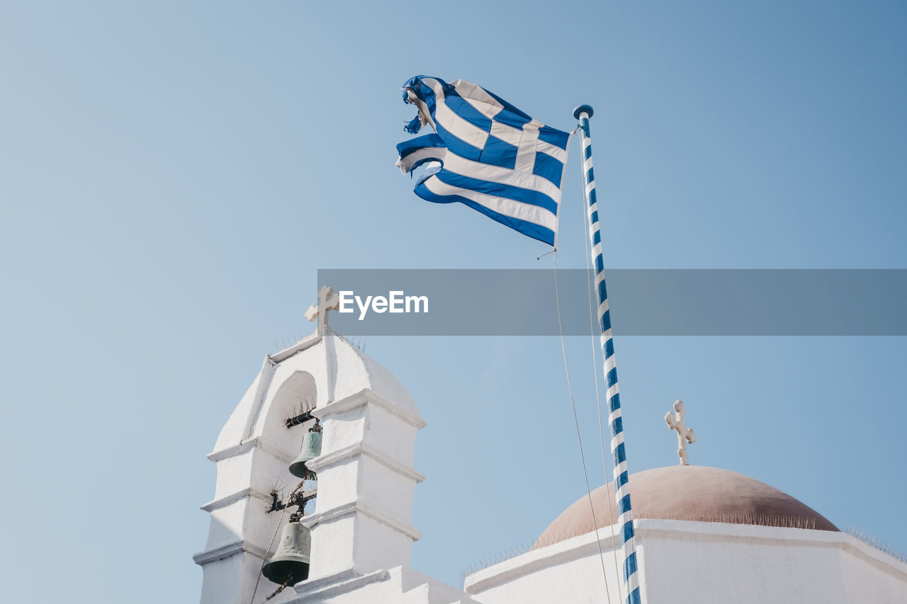 Low angle view of a greek flag on a traditional  whitewash building against clear blue sky