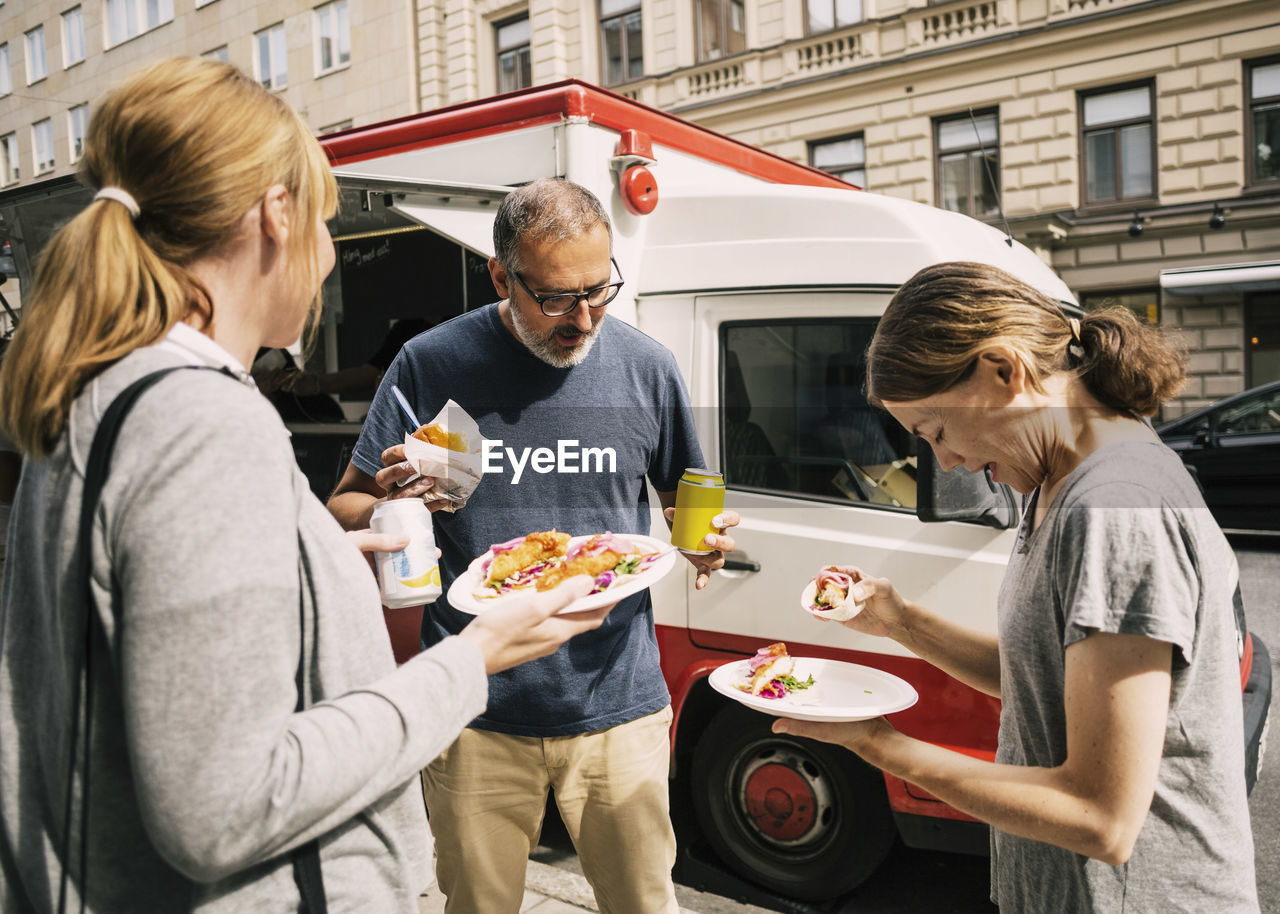 People eating food while standing by truck at city street