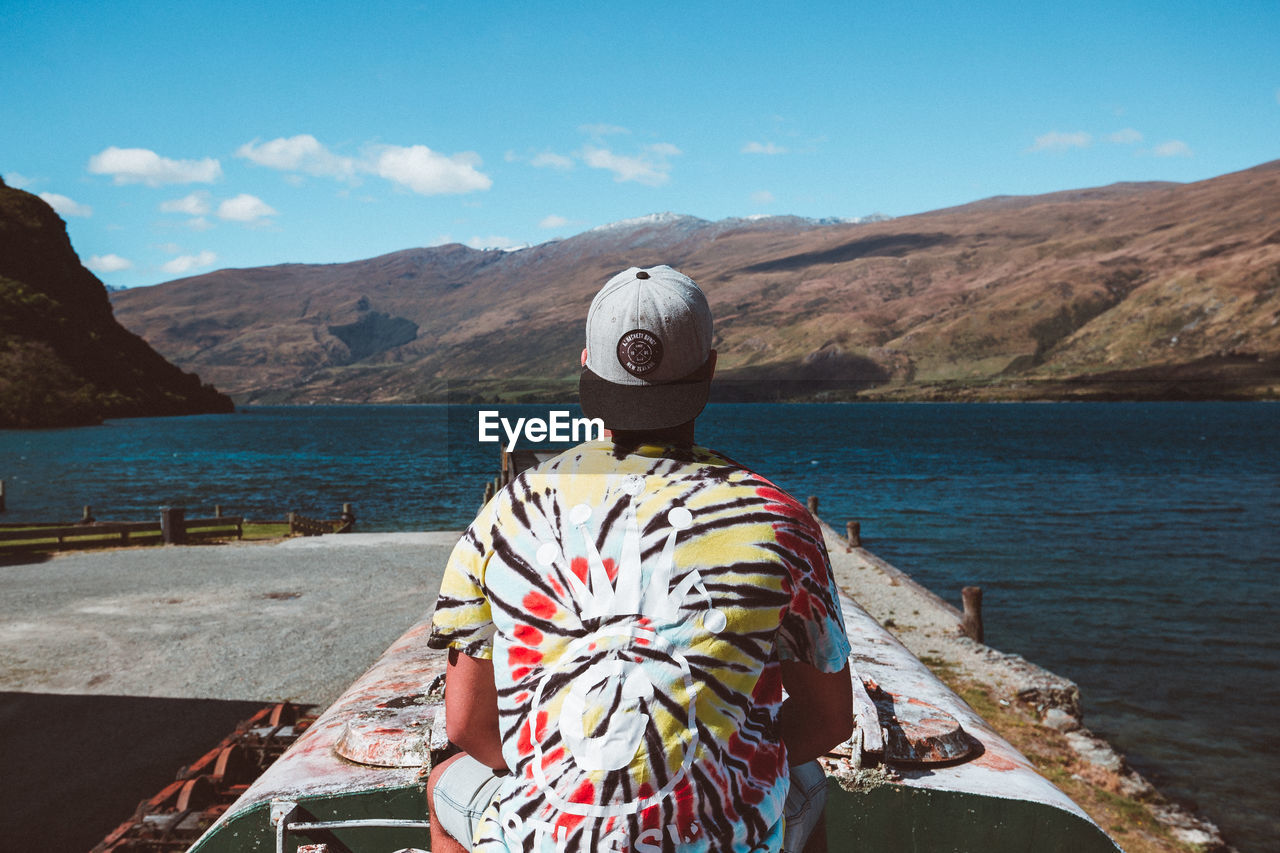 REAR VIEW OF A MAN OVERLOOKING SEA