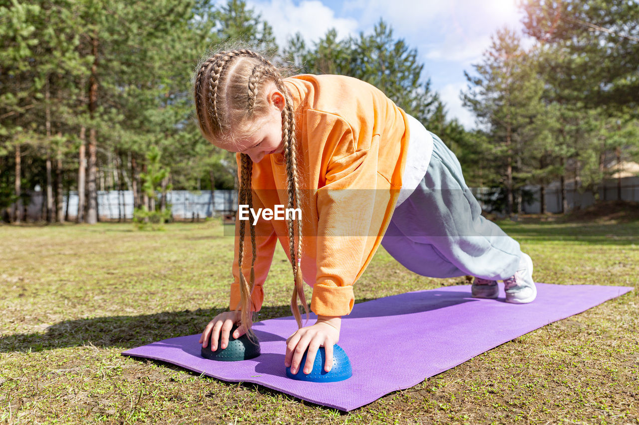 A teenage girl goes in for sports in nature, on a sunny summer day she does push-ups on a sports mat