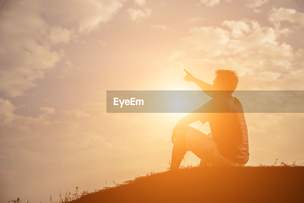 Side view of silhouette man sitting against sky during sunset