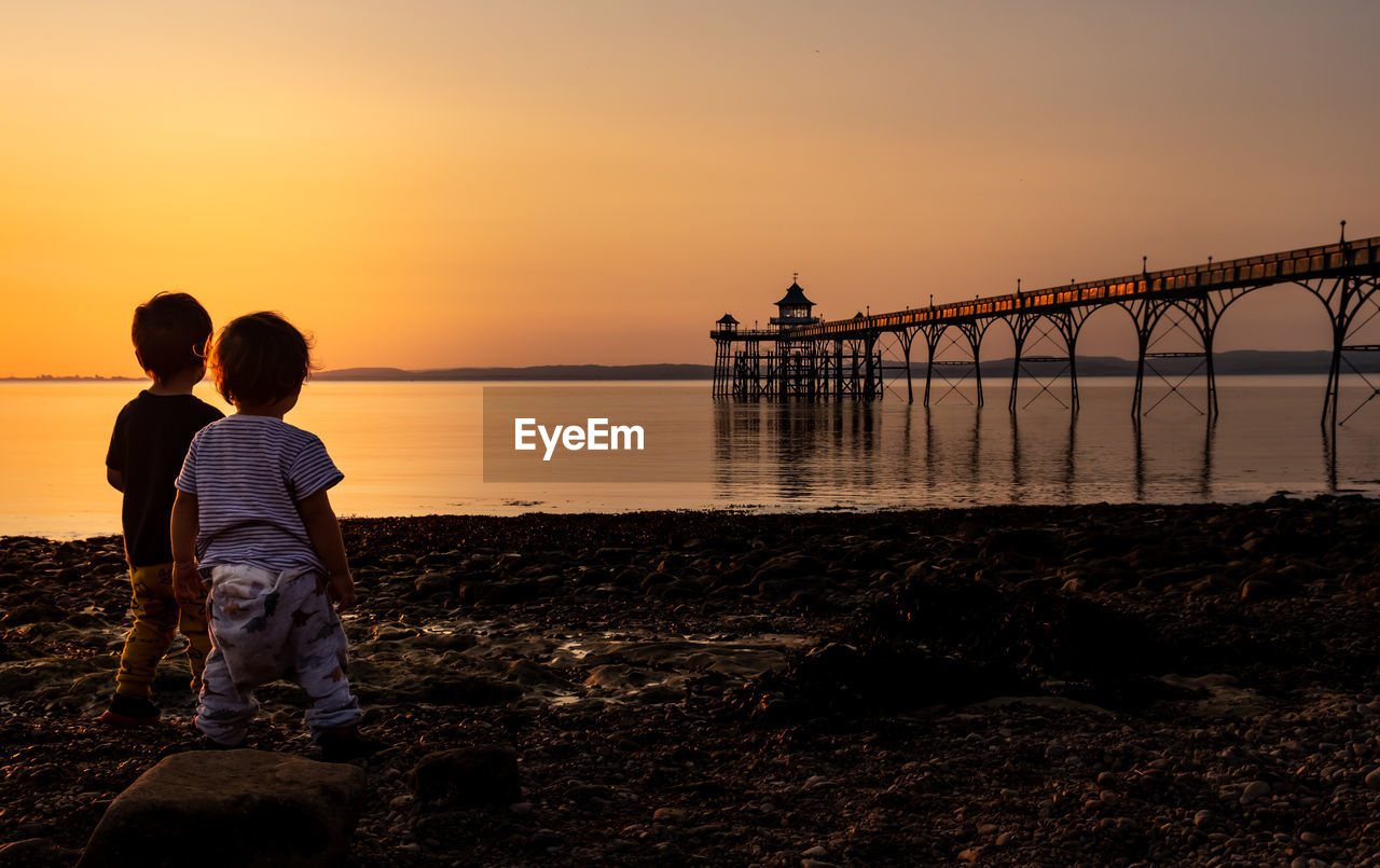 Rear view of children against sky during sunset with view of a pier